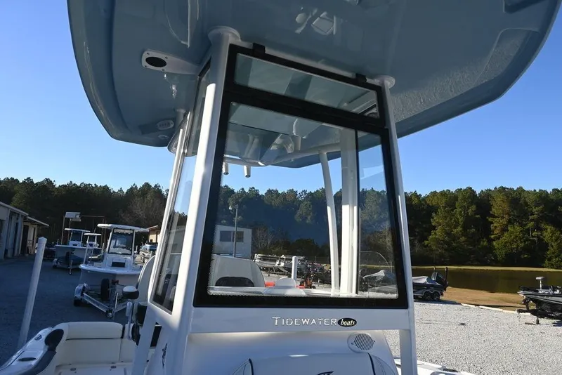 Slide: The Image of 2026 Tidewater 210 LXF boat with T-top, parked outdoors near trees and other boats. - 16