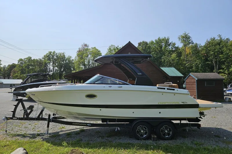 Slide: The Image of 2025 Chaparral 267 SSX boat on trailer, parked near wooden cabins and trees. - 4