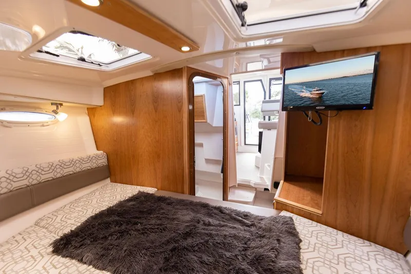 Slide: The Image of Interior of 2025 Cutwater C-288 Coupe LE, featuring cozy cabin with TV and plush bedding. - 27