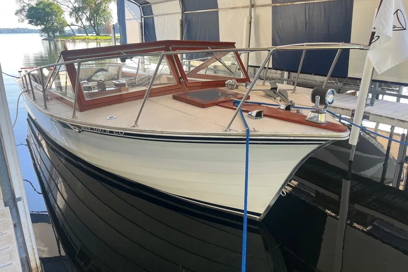 The Image of 1984 Skiff Craft 26 Runabout docked in a covered marina, reflecting on calm water. - 1