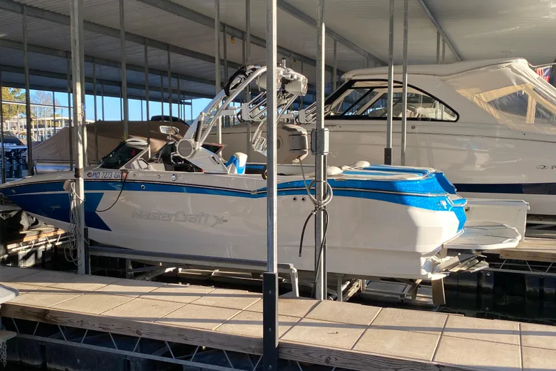 The Image of 2019 MasterCraft XStar boat docked in a marina, featuring blue and white design. - 2