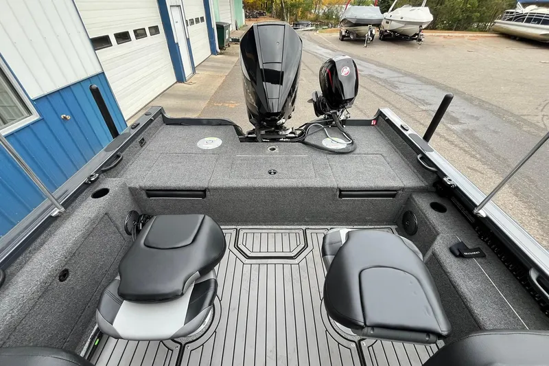 Slide: The Image of 2025 Crestliner 2050 Fish Hawk boat interior with seating and motor, docked near blue building. - 16