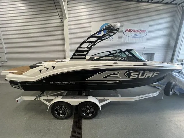 The Image of 2025 Chaparral 23 Surf boat on trailer in showroom, sleek design, black and white color scheme. - 0