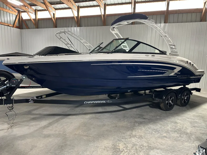 The Image of 2025 Chaparral 23 SSi boat in storage, featuring sleek blue and white design. - 1