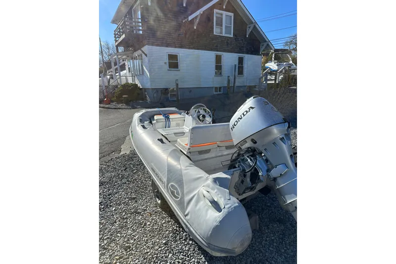 Slide: The Image of 2016 Walker Bay 325 ST inflatable boat with Honda motor, parked on gravel near a house. - 6