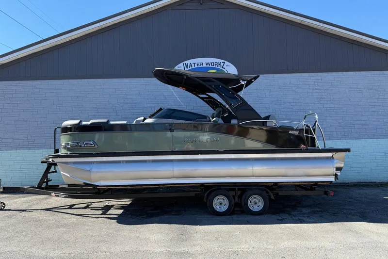 The Image of 2026 Avalon 2385 Catalina QLS Windshield pontoon boat on trailer, parked outside a building. - 1