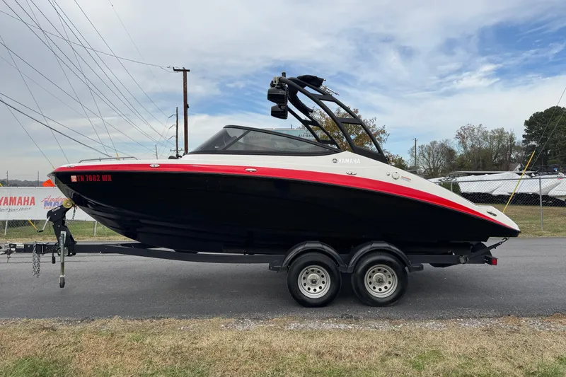 The Image of 2021 Yamaha AR210 boat on trailer, black and red design, parked outdoors. - 1