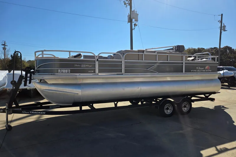 The Image of 2019 Sun Tracker Fishin' Barge 22 XP3 pontoon boat on trailer in outdoor setting. - 0