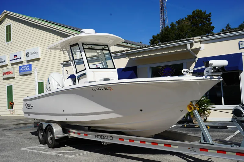 The Image of 2023 Robalo 266 Cayman boat on trailer outside dealership, sunny day. - 0