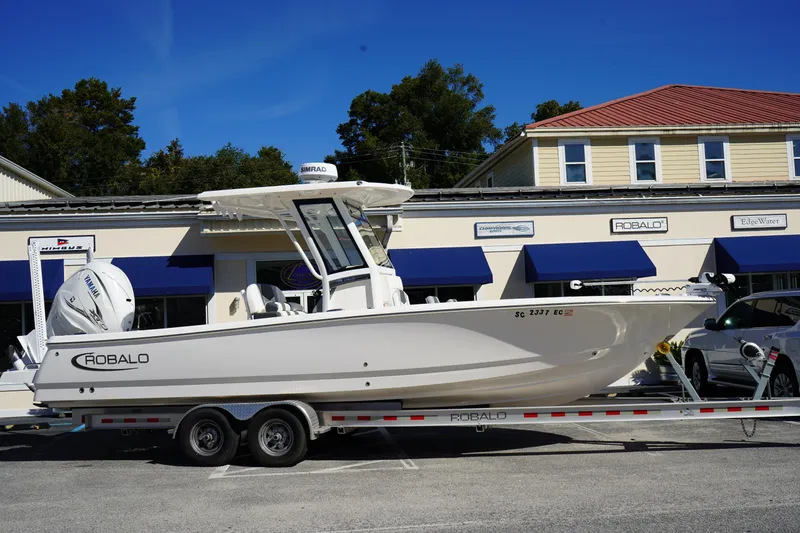 Slide: The Image of 2023 Robalo 266 Cayman boat on trailer outside dealership, clear sky background. - 1