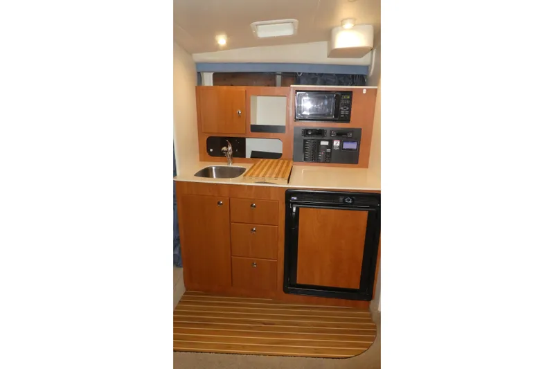 Slide: The Image of 2007 Bayliner 325 boat kitchen with sink, microwave, and wooden cabinetry. - 23