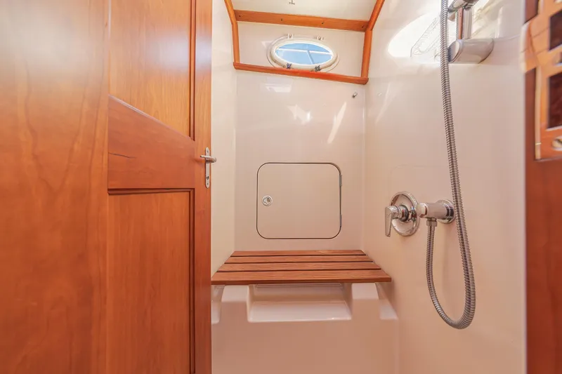 Slide: The Image of Hinckley Talaria 44 Express 1999 yacht shower with wooden bench and porthole window. - 48