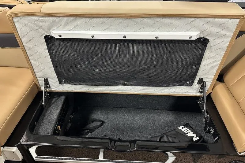 Slide: The Image of 2025 MasterCraft XT24 boat storage compartment with open lid and beige seating. - 30