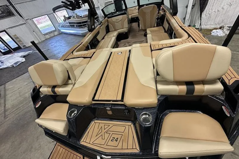 Slide: The Image of 2025 MasterCraft XT24 boat interior with tan seating and wood accents in a showroom. - 8