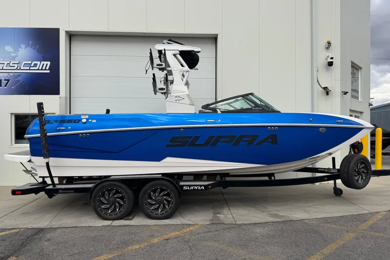 The Image of 2020 Supra SL 575 boat in vibrant blue on a trailer, parked outside a building. - 1