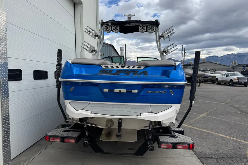 Slide: The Image of 2020 Supra SL 575 boat, blue and white, parked outside a garage. - 3