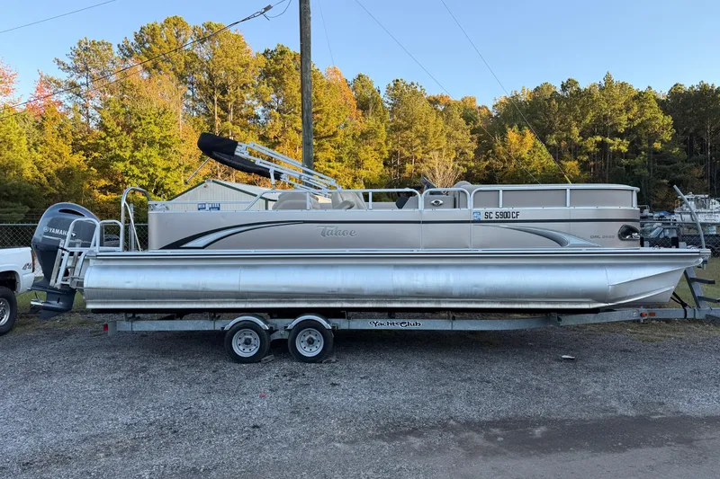 Slide: The Image of 2011 Tahoe Pontoon 2485 DRL on trailer, parked outdoors with trees in background. - 1