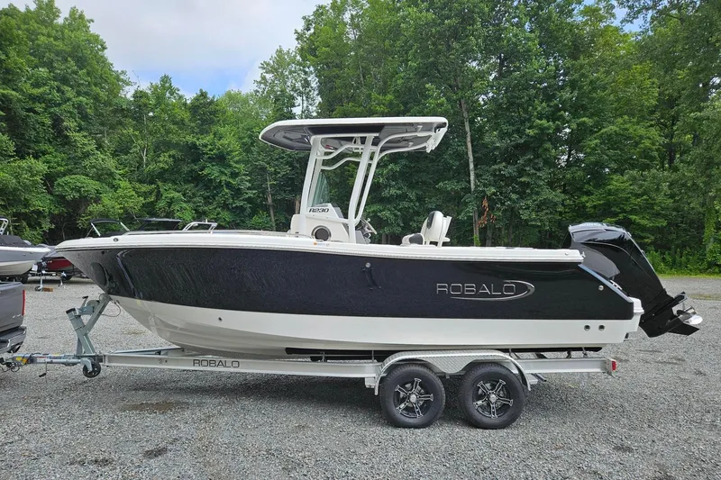 The Image of 2025 Robalo R230 Center Console boat on trailer, surrounded by lush greenery. - 0