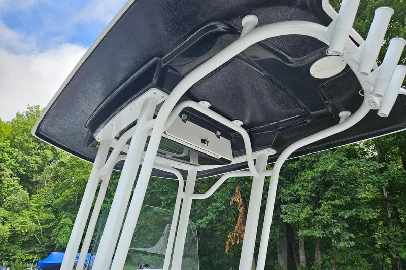 Slide: The Image of 2025 Robalo R230 Center Console T-top with rod holders, set against a forest backdrop. - 24