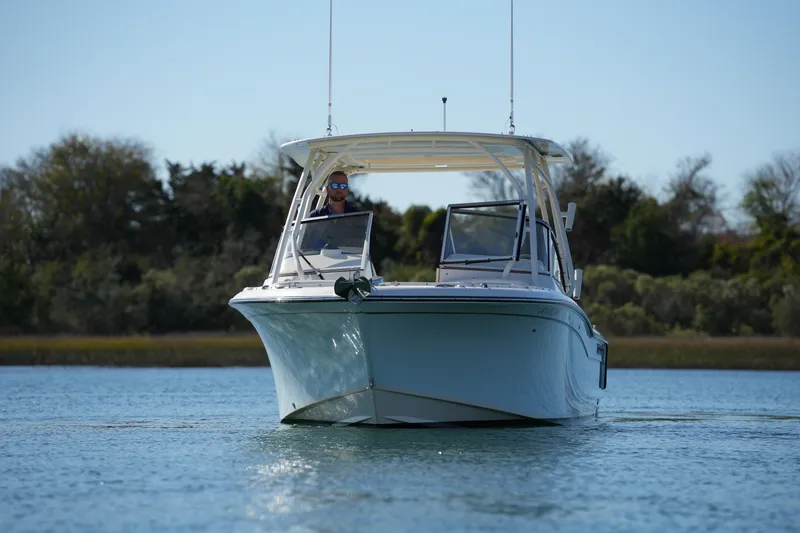 Slide: The Image of 2022 Grady-White Freedom 235 boat cruising on calm water with trees in the background. - 2