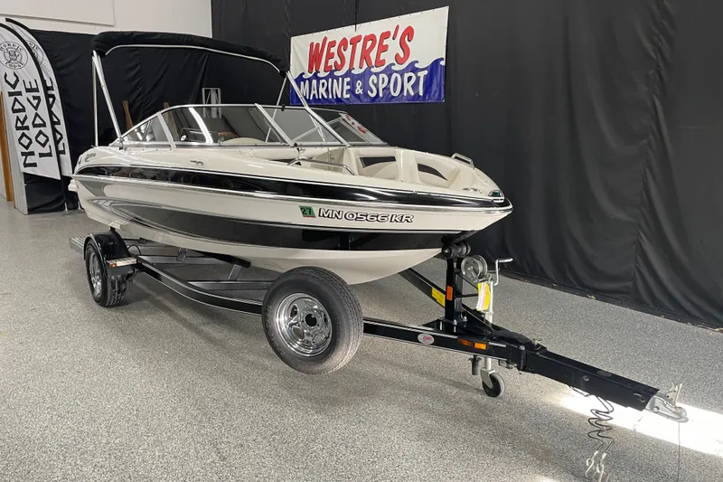 Slide: The Image of 2010 Glastron GT 185 boat on trailer in showroom, featuring sleek design and bimini top. - 2