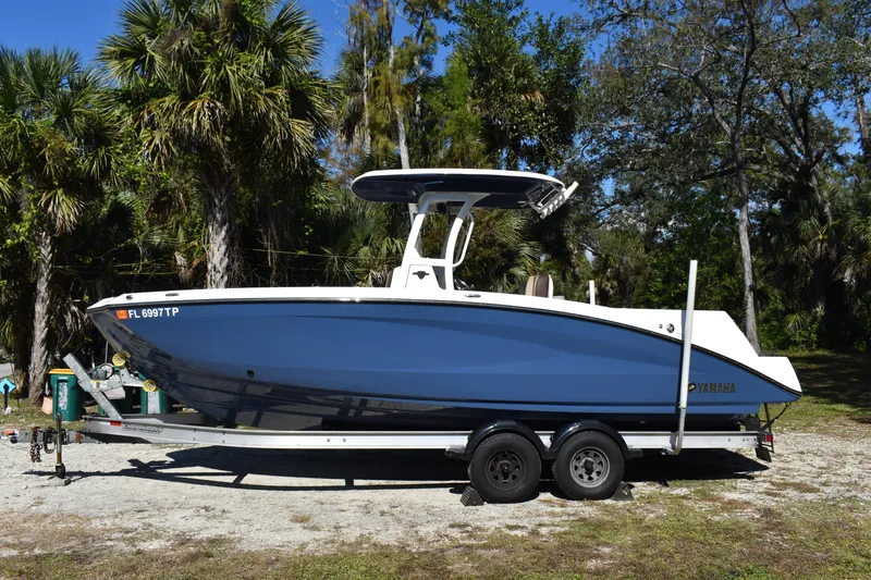 Slide: The Image of 2023 Yamaha Boats 252 FSH Sport, blue and white, on trailer under clear sky. - 5