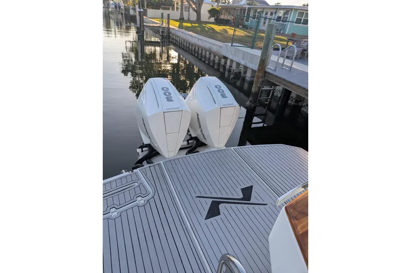 Slide: The Image of 2023 NX Boats 340 Sport Coupe with twin outboard engines docked by a canal. - 14