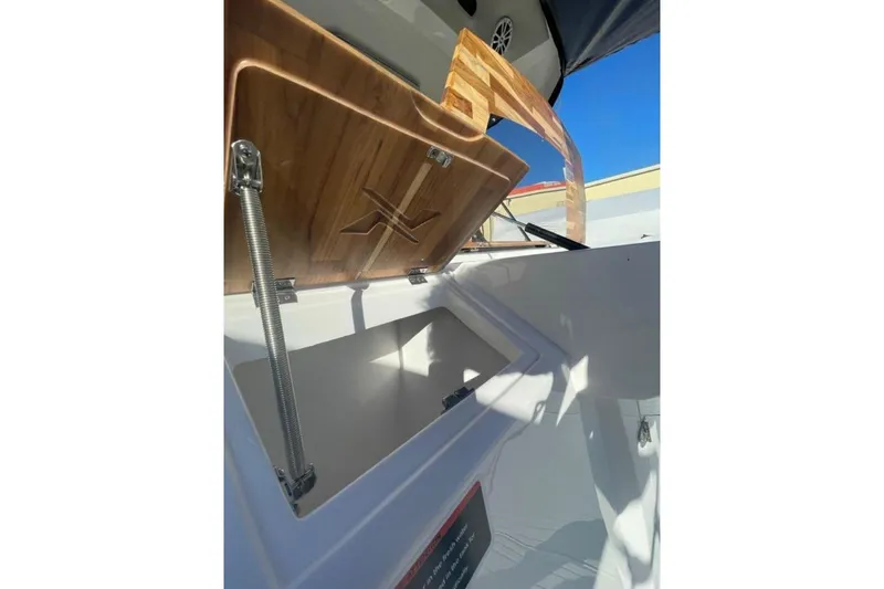 Slide: The Image of 2023 NX Boats 340 Sport Coupe storage compartment with wooden lid open under clear blue sky. - 19