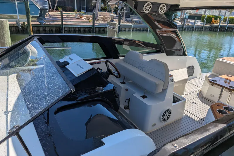 Slide: The Image of 2023 NX Boats 340 Sport Coupe cockpit with modern seating and controls, docked by the water. - 35