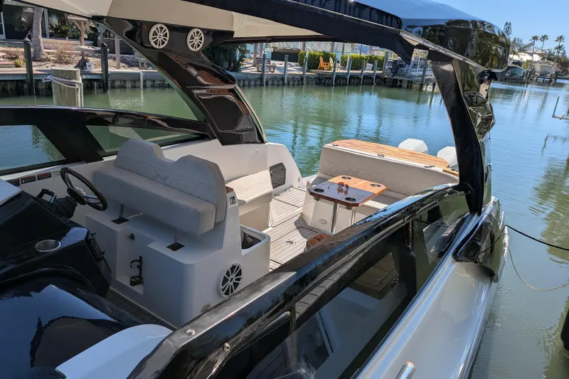 Slide: The Image of 2023 NX Boats 340 Sport Coupe interior with seating and table, docked by calm water. - 36