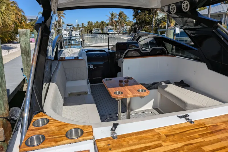 Slide: The Image of 2023 NX Boats 340 Sport Coupe interior with seating and wooden table, docked at marina. - 59