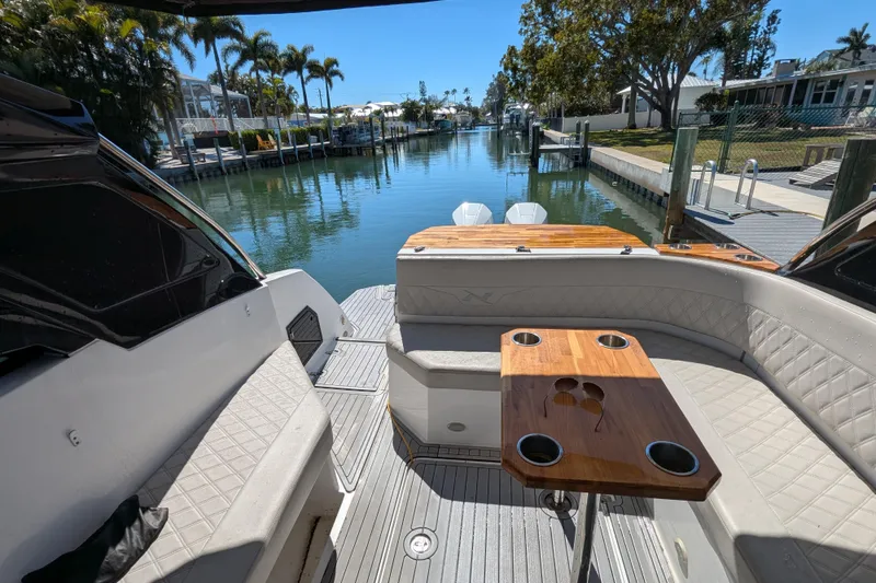 Slide: The Image of 2023 NX Boats 340 Sport Coupe interior with seating and table, docked by a scenic canal. - 70