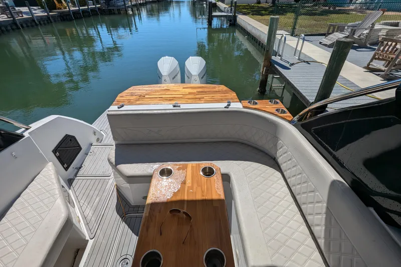 Slide: The Image of 2023 NX Boats 340 Sport Coupe interior with elegant seating and wooden table by the water. - 71