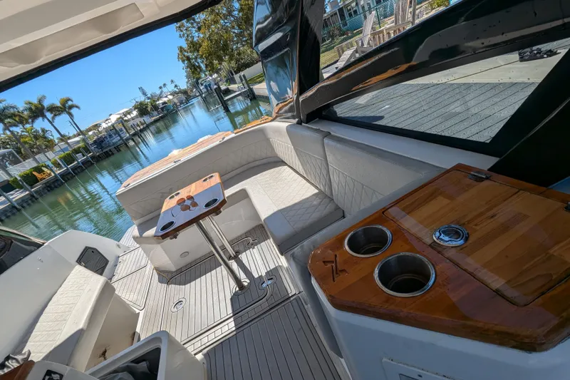 Slide: The Image of 2023 NX Boats 340 Sport Coupe interior with seating and table, overlooking a serene waterfront. - 72
