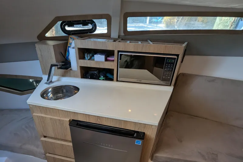 Slide: The Image of 2023 NX Boats 340 Sport Coupe interior with kitchenette, sink, microwave, and compact fridge. - 83