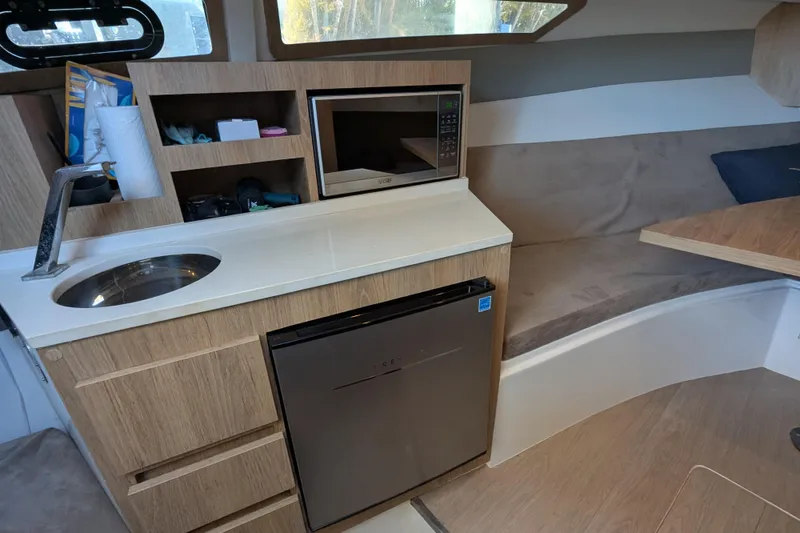 Slide: The Image of 2023 NX Boats 340 Sport Coupe interior with kitchenette, microwave, and seating area. - 85