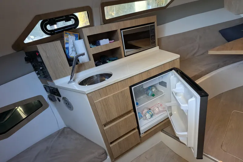 Slide: The Image of Interior of 2023 NX Boats 340 Sport Coupe with kitchenette and open mini fridge. - 88