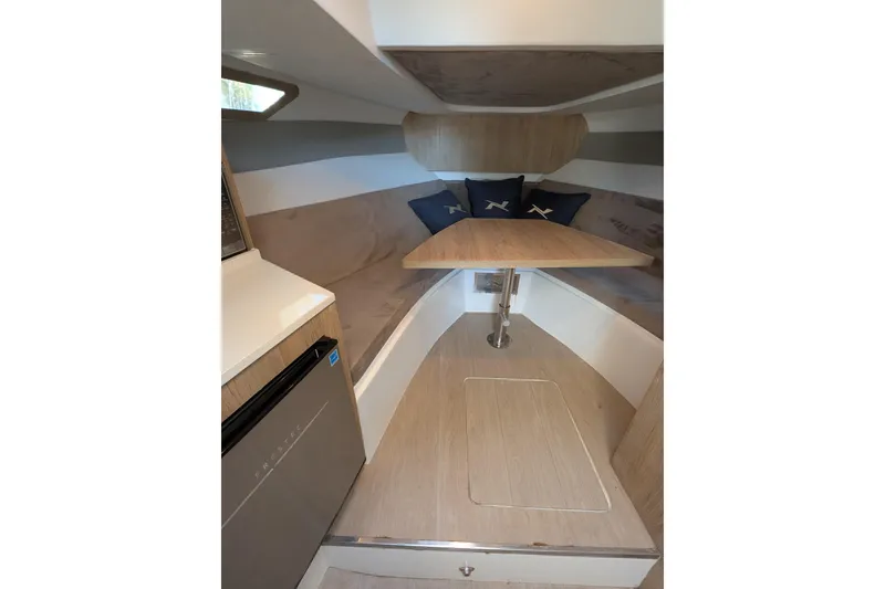 Slide: The Image of 2023 NX Boats 340 Sport Coupe interior with table, cushions, and compact fridge. - 98