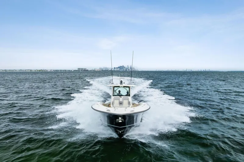 Slide: The Image of 2020 Scout 355 LXF boat cruising on open water with city skyline in background. - 10