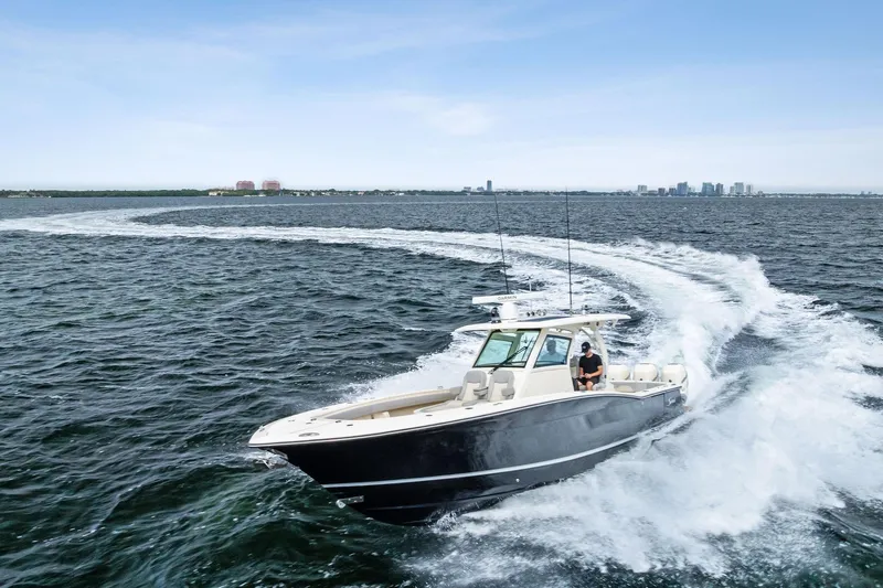Slide: The Image of 2020 Scout 355 LXF boat cruising on open water with city skyline in background. - 13