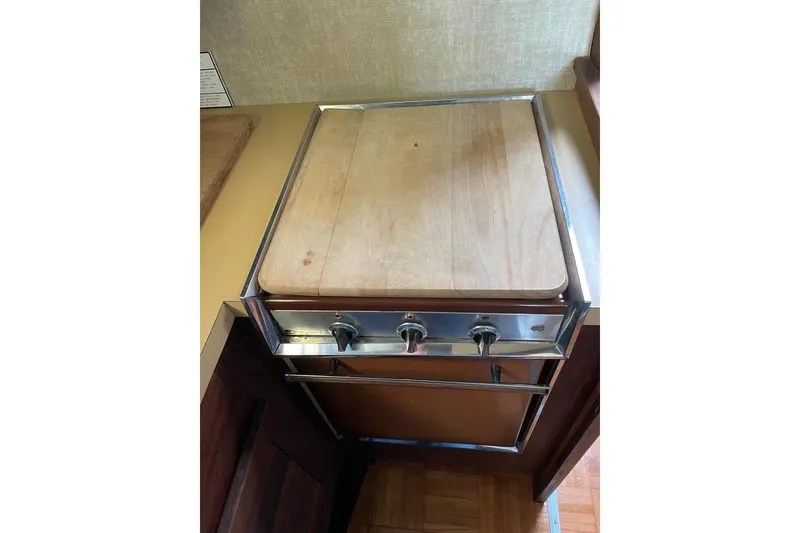 Slide: The Image of 1982 Mainship 34 MK 1 boat stove with wooden cover in compact kitchen area. - 22