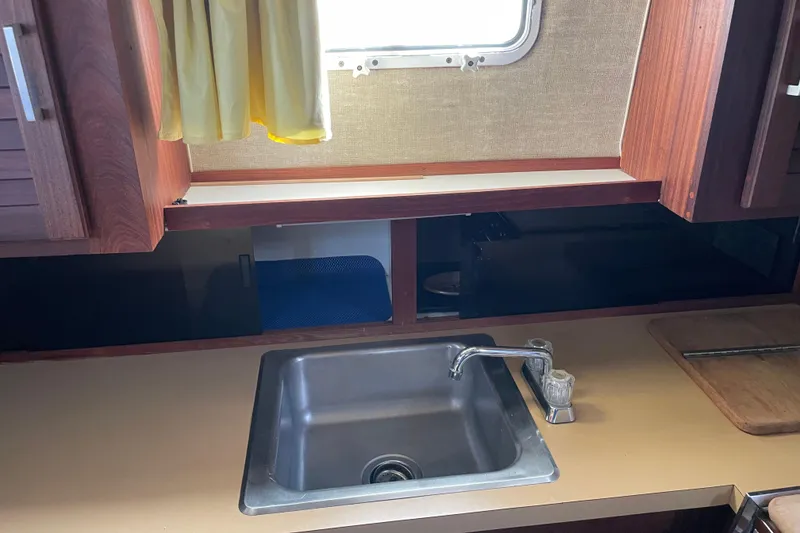 Slide: The Image of 1982 Mainship 34 MK 1 boat kitchen with sink, wooden cabinets, and yellow curtain. - 25