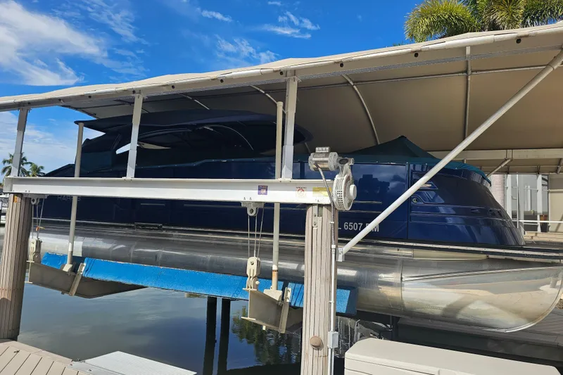 Slide: The Image of 2018 Harris V270 pontoon boat on lift, showing hull and pontoons above water. - 12