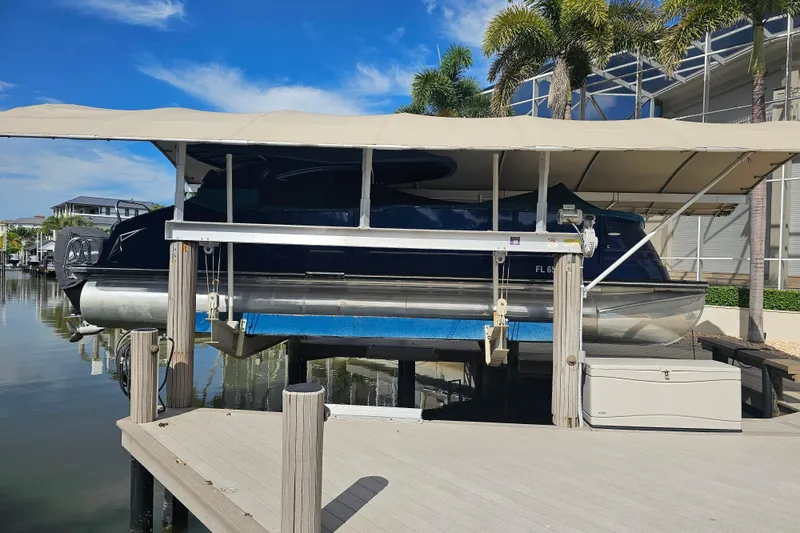 Slide: The Image of 2018 Harris V270 pontoon boat with blue cover, docked under a canopy. - 13