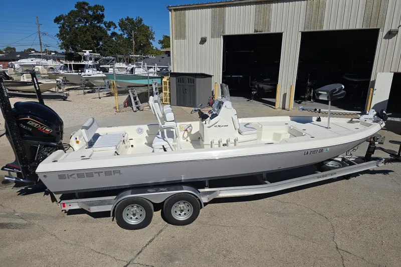 Slide: The Image of 2023 Skeeter SX230 boat on trailer, parked outside a warehouse. - 2