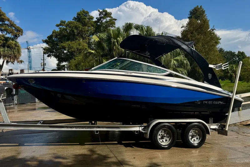 Slide: The Image of 2013 Regal 21 OBX boat on trailer, blue and white, parked outdoors. - 21