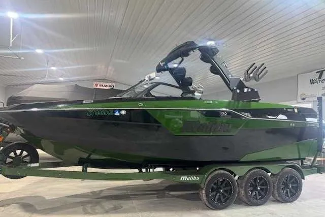 Slide: The Image of 2022 Malibu M240 boat in a showroom, black and green design, on a trailer. - 1