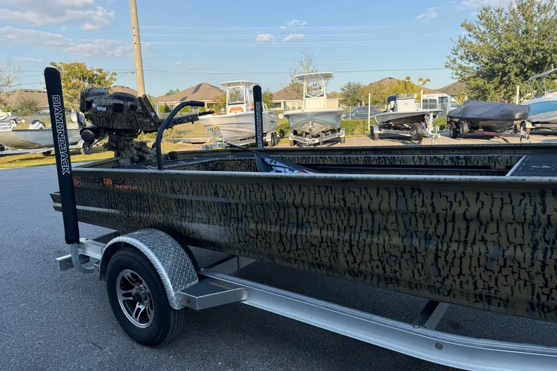 Slide: The Image of 2025 Diamondback Mud Rattler 1860 boat on trailer, camo design, parked outdoors. - 3