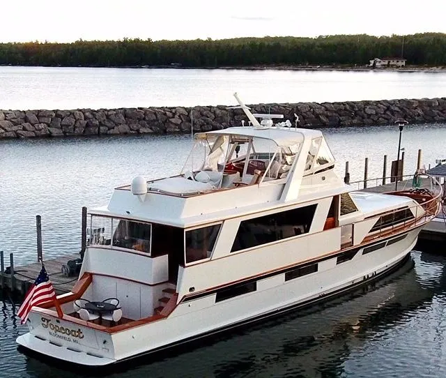 Slide: The Image of 1974 Pacemaker Cockpit Motoryacht docked by a stone breakwater, displaying an American flag. - 1