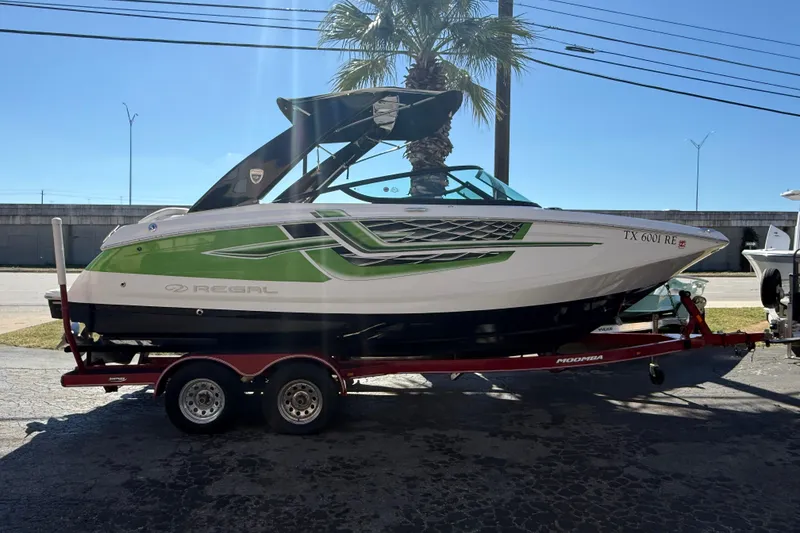 The Image of 2018 Regal 22 FasDeck boat on trailer, green and white design, parked outdoors. - 1